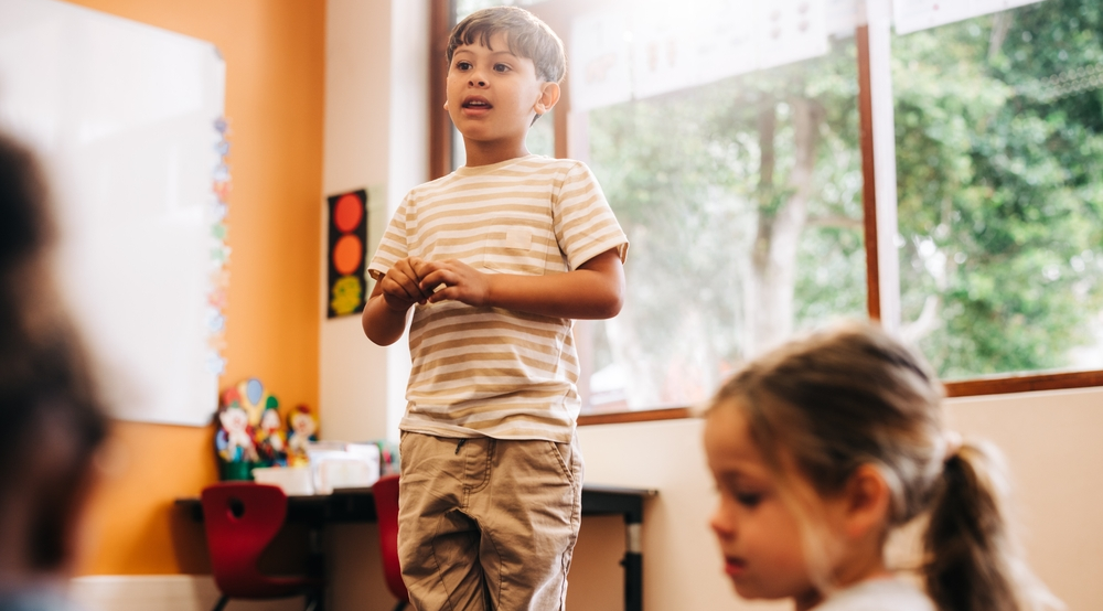 Niño asertiva habla al frente de su salón de clases