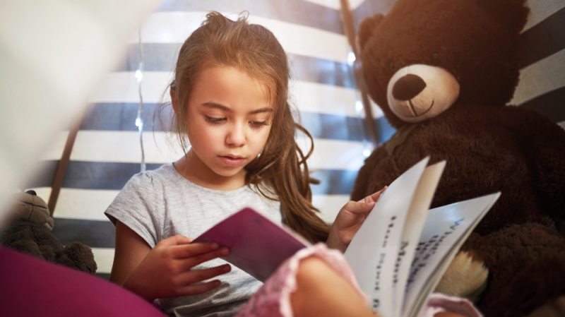 Niña aprende a leer sentada junto a peluche