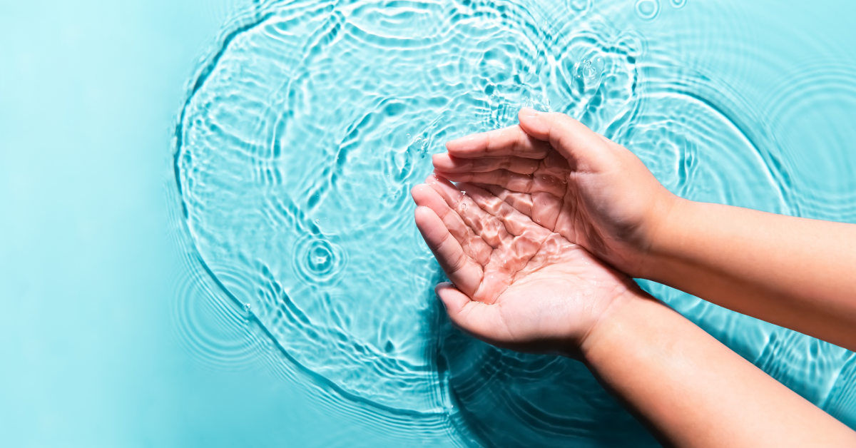 Manos de niño que sostienen agua en fondo azul